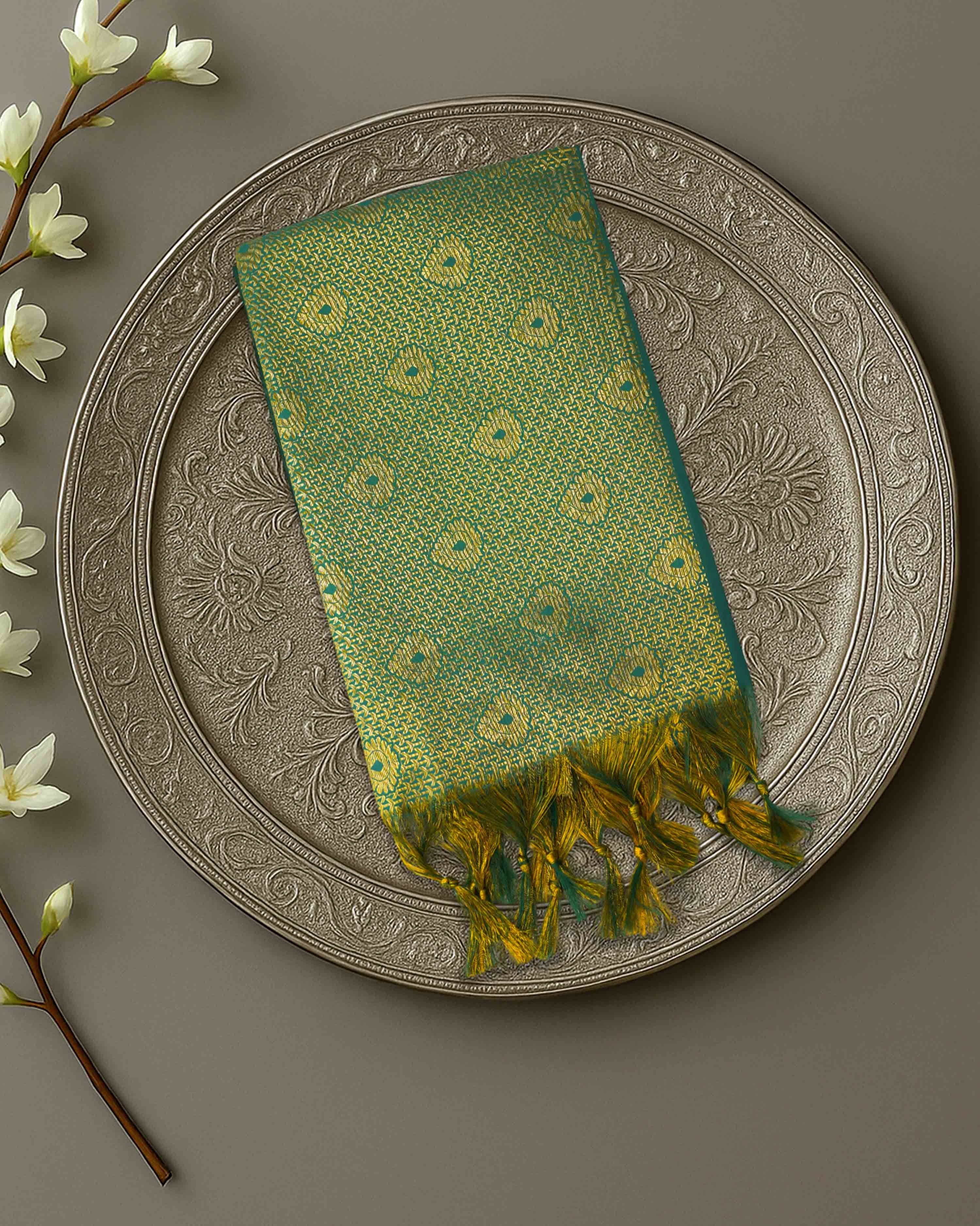 Ambika Stores green and gold zari Ponnadai shawl with traditional patterns and tassel edges on a decorative plate.
